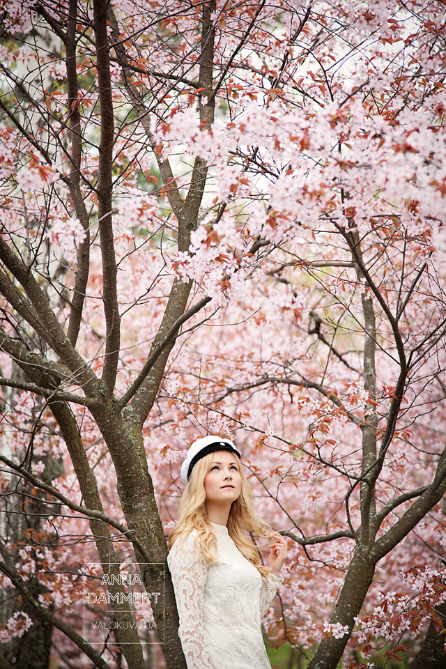 Ylioppilaskuva nuoresta naisesta kukkivien kirsikkapuiden alla