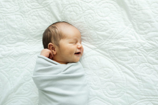 Pieni-vauva-hymyilee-unissaan-sängyllä-kapaloituna